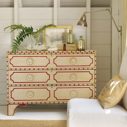 Decorative chest of drawers with red accents in a room with a plant and lamp.