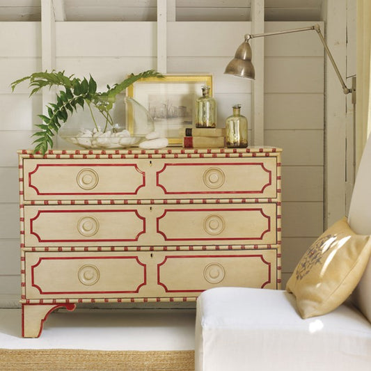Decorative chest of drawers with red accents in a room with a plant and lamp.